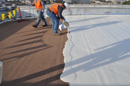 Commercial roof surface prepared with white coating and buckets of adhesive during deck installation.